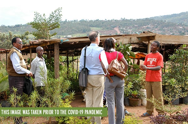 PMC staffers interviewing a young man at his tree farm in Rwanda. The area is full of greenery and mountain villages in the background.