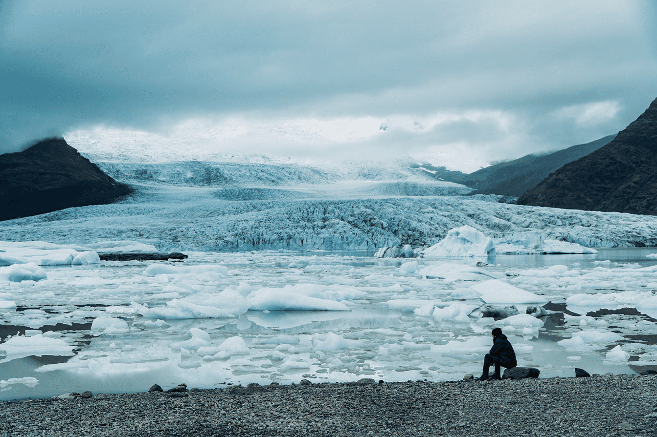 Man sits in front of melting glacier on a grey day.