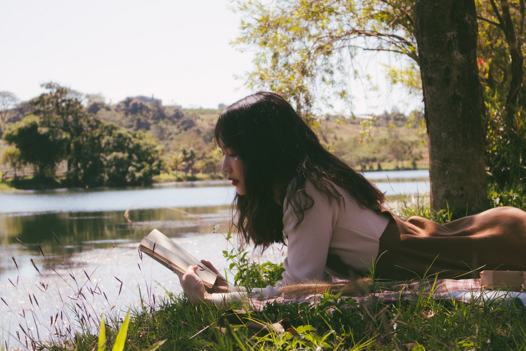 Woman reading by a river. Photo by Nguyen Thu Hoai on Unsplash.