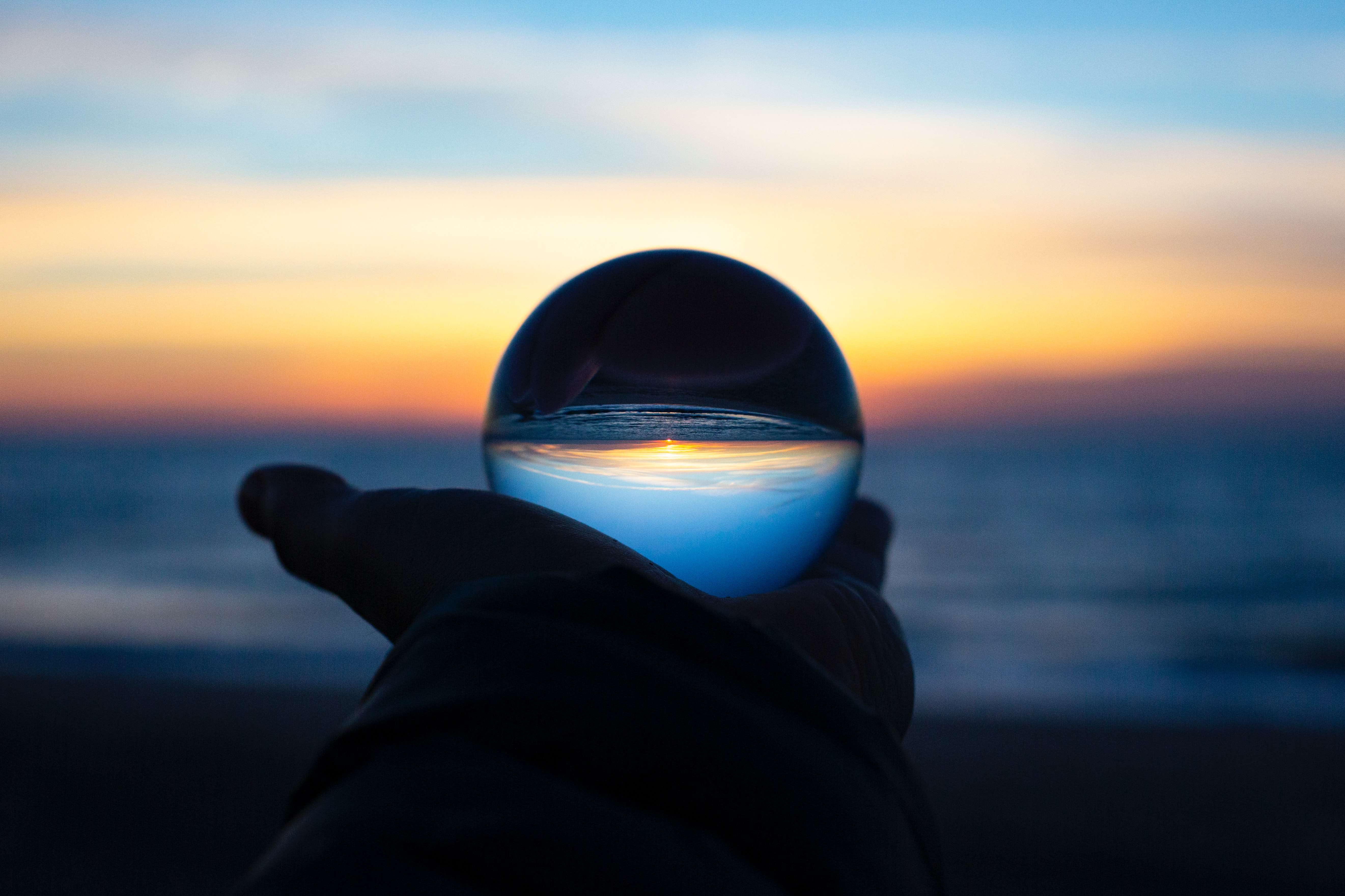 Hand holding a glass ball by the ocean at sunrise